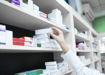 Closeup View Of Pharmacist Hand Taking Medicine Box From The Shelf In Drug Store.