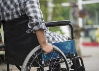 Close Up Of Senior Woman Hand On Wheel Of Wheelchair During Walk